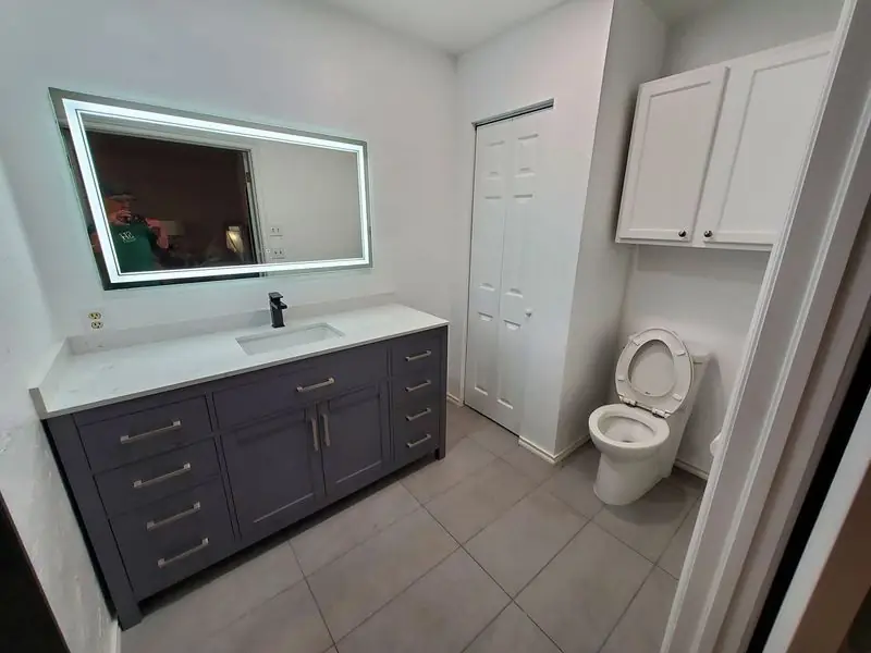 Bathroom remodel with dark grey vanity, backlit mirror and tile floor