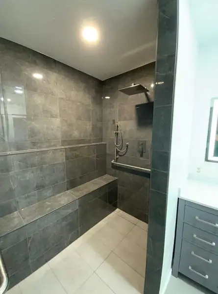 Walk-in shower stripped back and rebuilt in dark stone-look tile with a built-in bench