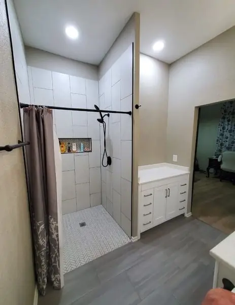 Tiled walk-in shower with herringbone floor tile beside a white vanity