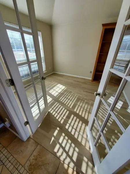 French doors opening onto a finished room with light wood flooring and built-in shelving
