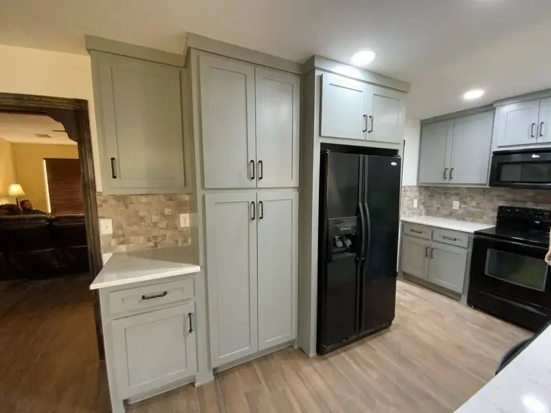Finished kitchen remodel with sage-grey cabinets, black appliances and a stacked-stone backsplash