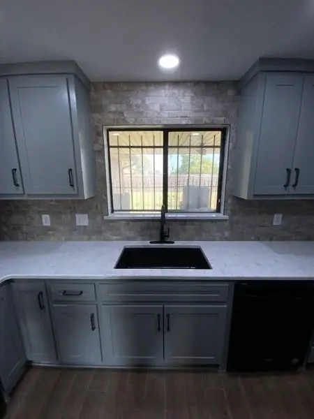 Kitchen sink under a window with stacked-stone backsplash and quartz countertop