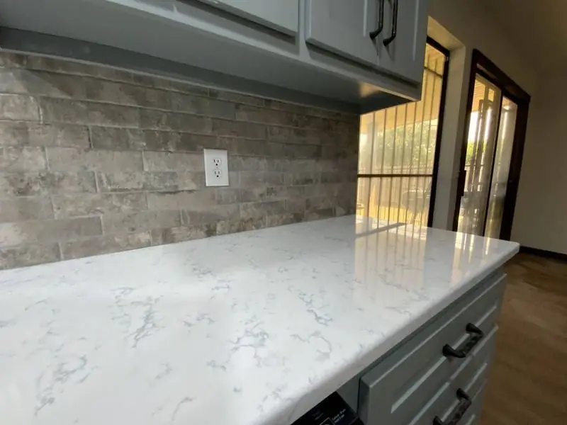 Quartz countertop and stacked-stone backsplash beside a patio door