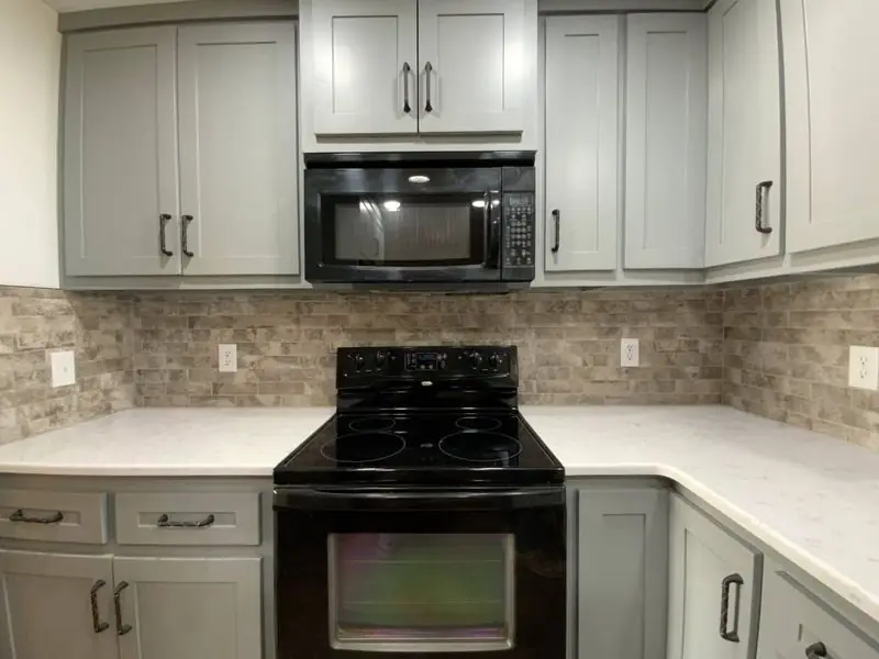 Kitchen range and microwave wall with stacked-stone backsplash and quartz counter